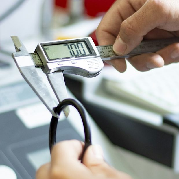 Reproduction de pièces Une main tenant un pied à coulisse numérique sur un plan de travail.