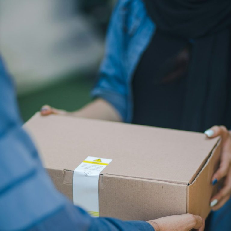 Vente d'articles Une personne remet un colis marron à une autre, dans un environnement extérieur.